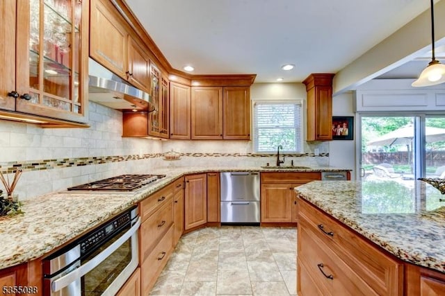 kitchen featuring decorative backsplash, under cabinet range hood, light stone counters, a sink, and stainless steel appliances