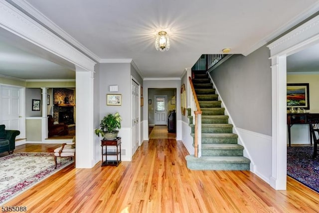 entryway featuring stairs, crown molding, decorative columns, and light wood-style floors