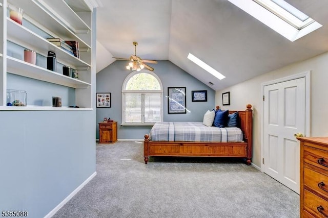carpeted bedroom featuring baseboards, ceiling fan, and vaulted ceiling with skylight