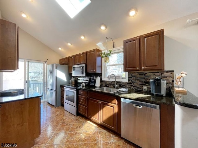 kitchen featuring decorative backsplash, appliances with stainless steel finishes, vaulted ceiling, a sink, and dark stone countertops