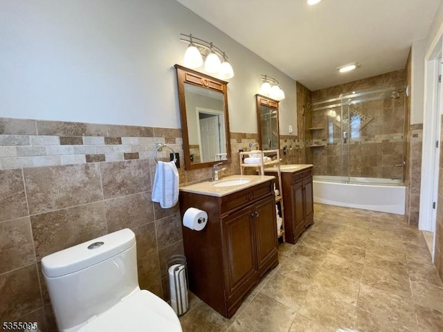 bathroom with vanity, combined bath / shower with glass door, toilet, and tile walls