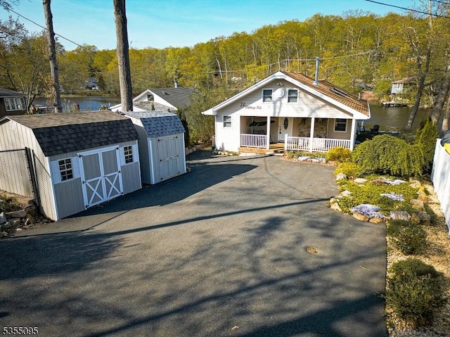 view of front of house with a storage unit, a porch, a view of trees, an outbuilding, and a water view