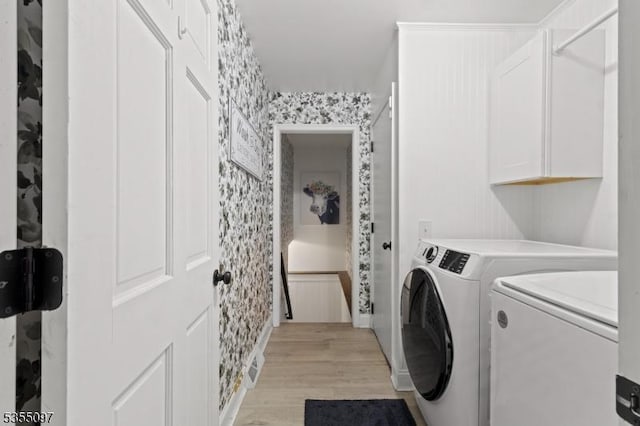 clothes washing area with separate washer and dryer, light wood-type flooring, wallpapered walls, and cabinet space