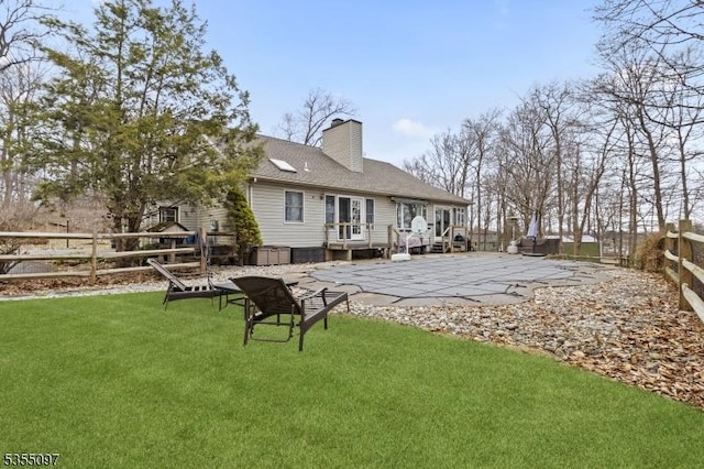 rear view of house with a deck, a fenced backyard, a chimney, a patio area, and a yard