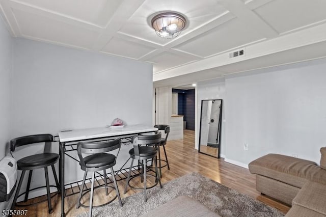 dining space featuring baseboards, visible vents, light wood finished floors, and coffered ceiling