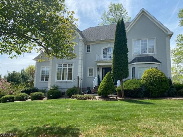 view of front of house featuring stucco siding, a balcony, roof with shingles, and a front lawn