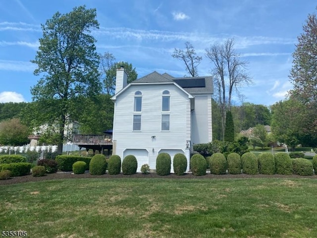 view of side of property featuring an attached garage, a chimney, a yard, and solar panels