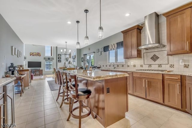 kitchen featuring open floor plan, a kitchen breakfast bar, wall chimney range hood, and tasteful backsplash