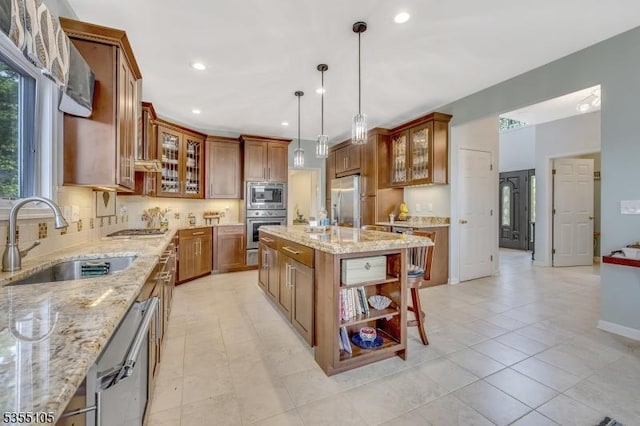 kitchen featuring brown cabinets, appliances with stainless steel finishes, light stone counters, a sink, and a center island