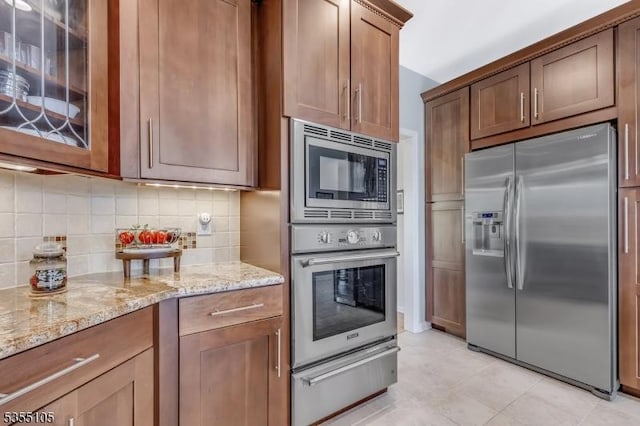 kitchen with decorative backsplash, light stone counters, glass insert cabinets, a warming drawer, and stainless steel appliances