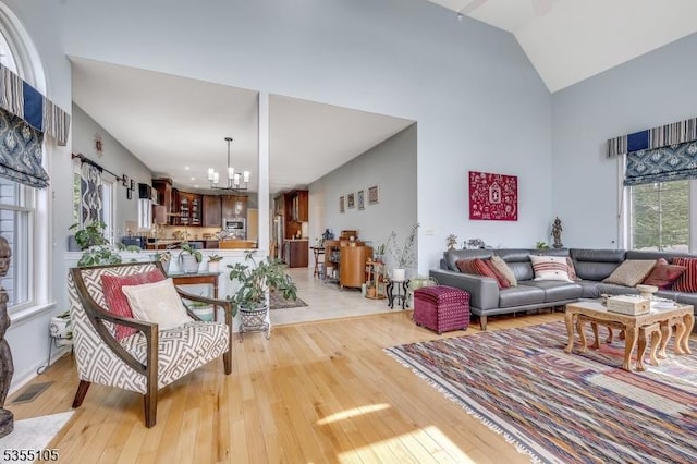 living room with high vaulted ceiling, visible vents, light wood-style flooring, and a chandelier