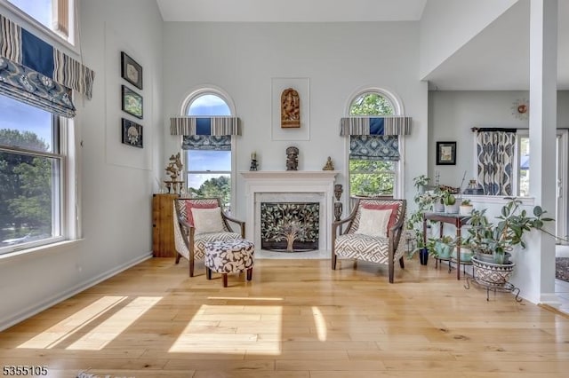 sitting room featuring wood-type flooring, baseboards, a fireplace with flush hearth, and a high ceiling