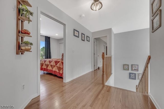 hall featuring baseboards, wood finished floors, and an upstairs landing