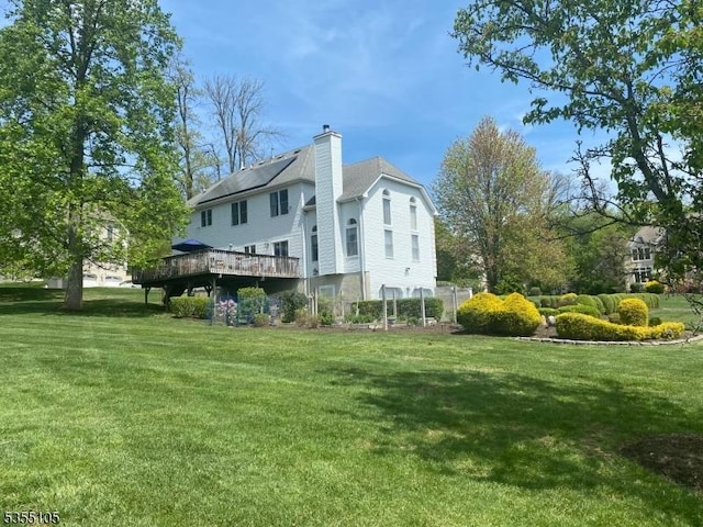 view of side of property featuring a yard, a deck, a chimney, and roof mounted solar panels