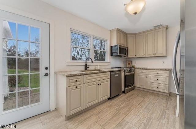 kitchen featuring a sink, appliances with stainless steel finishes, cream cabinetry, light stone counters, and light wood-type flooring