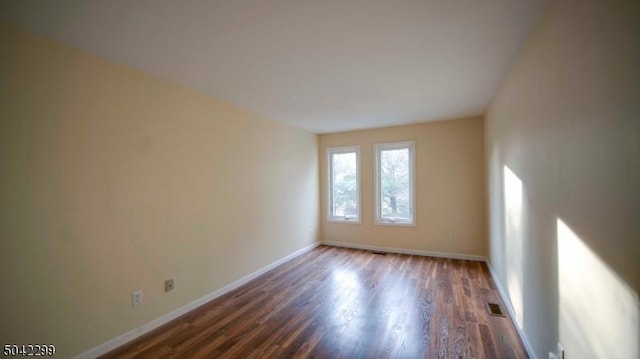 spare room featuring baseboards, visible vents, and dark wood-type flooring