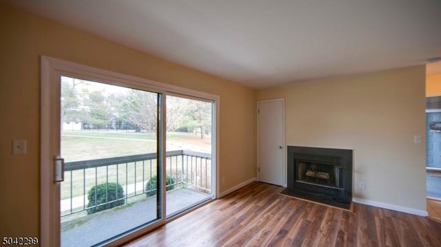 unfurnished living room featuring baseboards, a fireplace with flush hearth, and wood finished floors