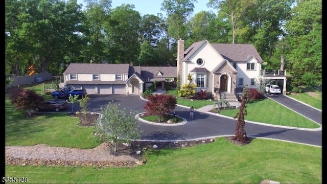 view of front of property featuring a chimney, a front lawn, driveway, and view of scattered trees