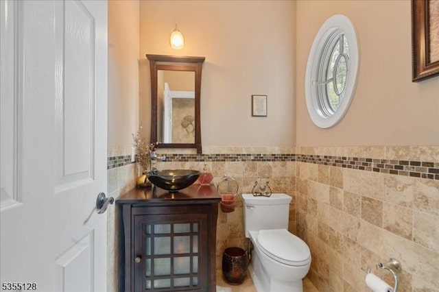 bathroom with tile walls, toilet, a wainscoted wall, and vanity