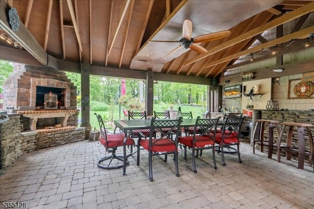 view of patio with an outdoor stone fireplace, ceiling fan, outdoor dining space, and a bar
