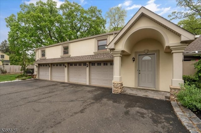entrance to property featuring stucco siding, asphalt driveway, stone siding, and a garage