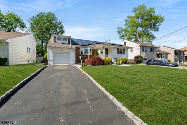 ranch-style home featuring a garage, solar panels, a front yard, and aphalt driveway