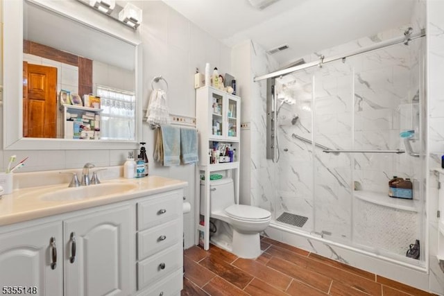 bathroom featuring toilet, wood finish floors, a marble finish shower, and vanity