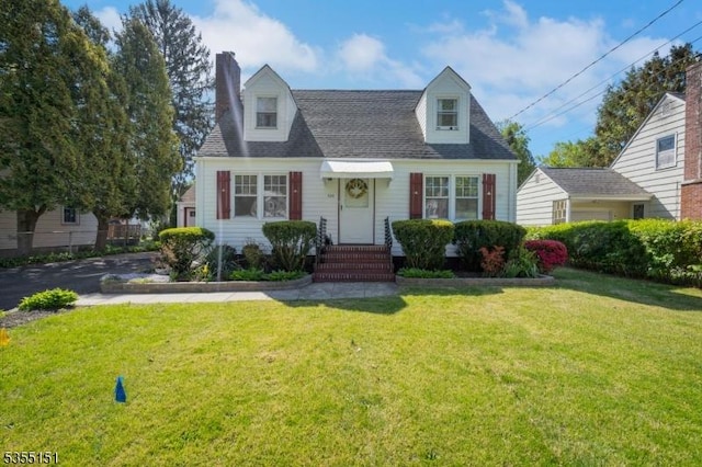 new england style home featuring roof with shingles, a chimney, and a front lawn