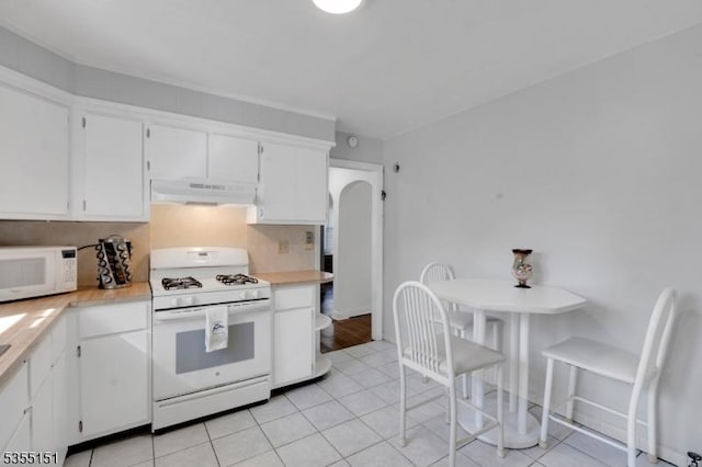 kitchen featuring arched walkways, light countertops, white cabinets, under cabinet range hood, and white appliances