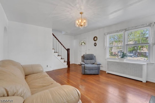 living room featuring stairs, wood finished floors, baseboards, radiator heating unit, and a notable chandelier