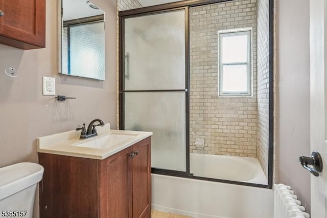 full bath with radiator heating unit, vanity, bath / shower combo with glass door, and toilet