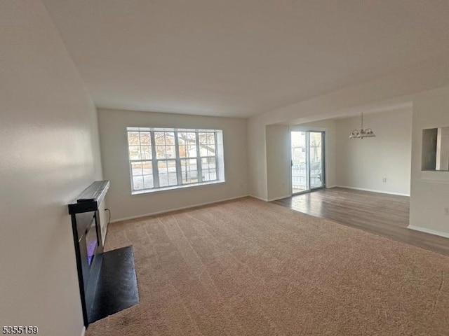 unfurnished living room with baseboards, plenty of natural light, carpet, and wood finished floors