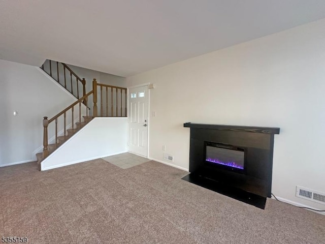 unfurnished living room with stairs, visible vents, a fireplace with flush hearth, and carpet