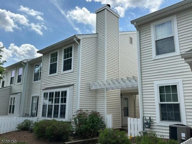 rear view of house with fence, a chimney, and cooling unit