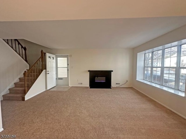 unfurnished living room featuring baseboards, a glass covered fireplace, carpet floors, and stairway
