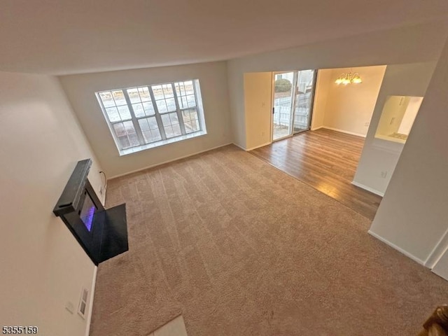 unfurnished living room with baseboards, carpet flooring, and a notable chandelier