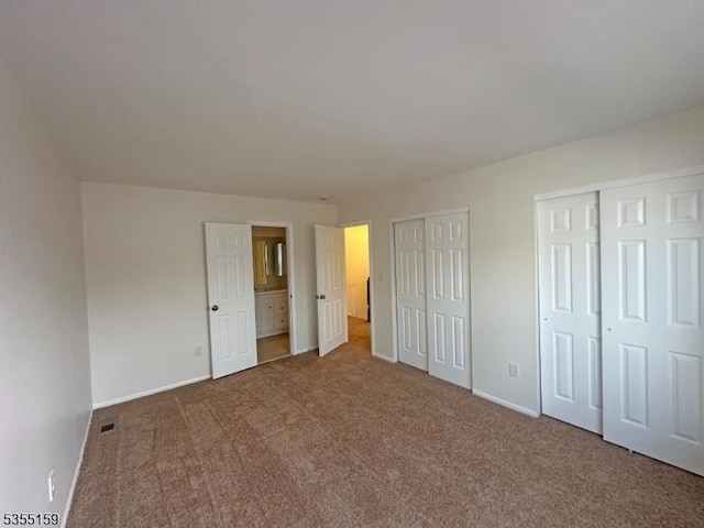 unfurnished bedroom with baseboards, carpet flooring, two closets, and visible vents