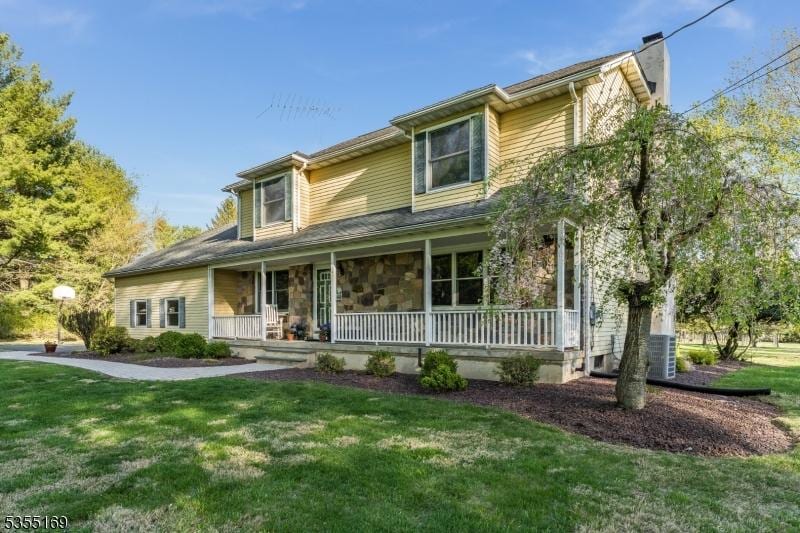 view of front of home featuring a porch, a front lawn, a chimney, and cooling unit