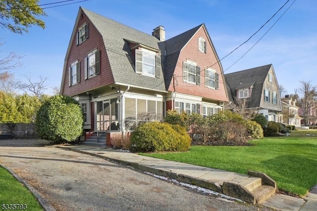 view of front of property featuring roof with shingles, a chimney, a gambrel roof, and a front yard