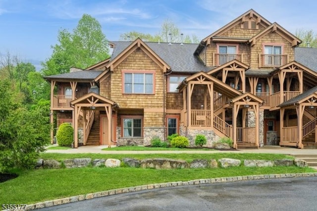 view of front of home with stairs, a front lawn, stone siding, and a balcony