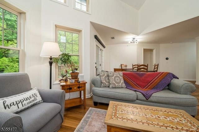 living room featuring a towering ceiling, visible vents, a healthy amount of sunlight, and wood finished floors