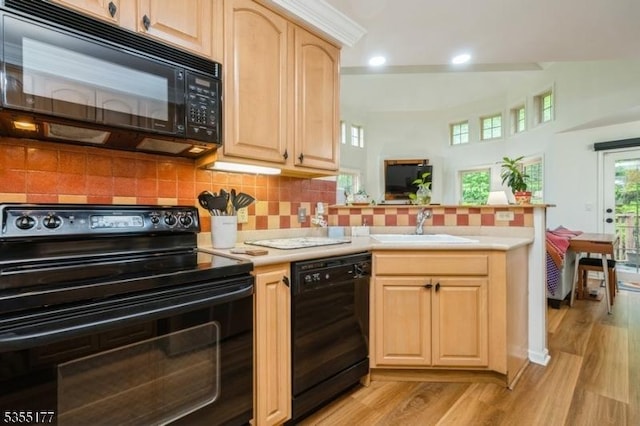 kitchen featuring a peninsula, light wood finished floors, a sink, light brown cabinetry, and black appliances