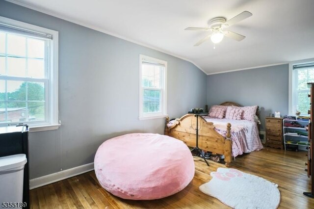 bedroom featuring wood finished floors, vaulted ceiling, ornamental molding, baseboards, and ceiling fan