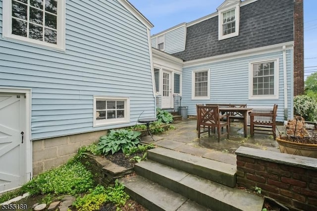 back of property with a shingled roof, a patio area, and outdoor dining space