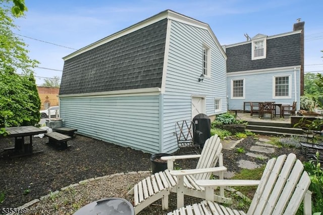 rear view of property with a shingled roof, a chimney, a deck, and a gambrel roof