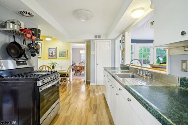 kitchen featuring stainless steel gas range oven, a sink, white cabinetry, stainless steel counters, and light wood-style flooring