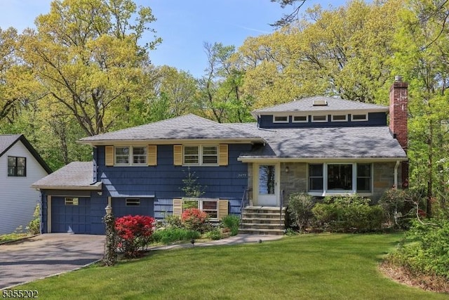 split level home featuring a garage, a front lawn, a chimney, a shingled roof, and driveway