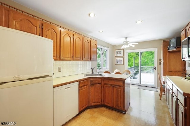kitchen with a ceiling fan, a peninsula, white appliances, light countertops, and a sink