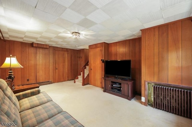 carpeted living area featuring a baseboard radiator, radiator heating unit, wooden walls, and stairway