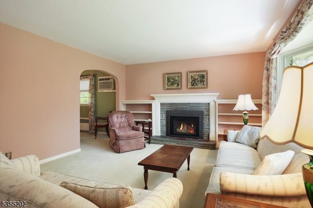 living room with carpet floors, baseboards, a warm lit fireplace, a wall mounted AC, and arched walkways